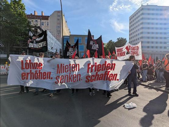 Das Foto von © Sabine Scheffer zeigt das  Fronttransparent mit der Losung „Löhne erhöhen, Mieten senken, Frieden schaffen“ und dahinter laufende Menschen. Im HIntergrund sind weitere Transparente zu sehen.