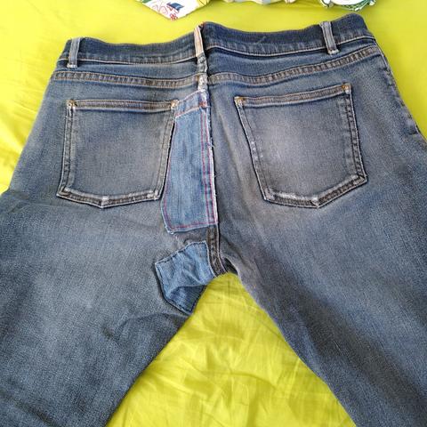 Face arrière d'un jeans bleu foncé très usé avec des réparations visibles en denim d'une autre nuance de bleu, sur les fesses.