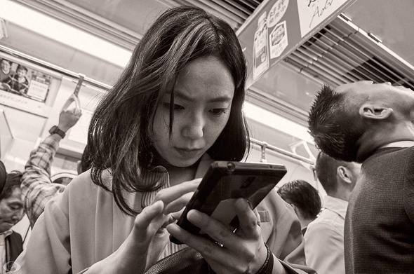 Packed train with a young Japanese woman focused on her smartphone.