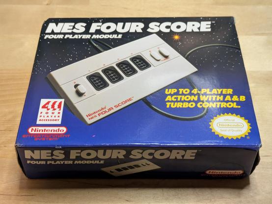 A photo of the box of the NES Four Score, a four port controller adapter for the Nintendo Entertainment System. The photo on the box shows a tan plastic box with four 7-pin sockets for NES controllers and a couple of buttons and switches for configuration. The tag line reads "up to 4-player action with A & B turbo control".