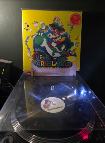 Artwork from super mario world featuring caped mario riding yoshi. A black vinyl is spinning below