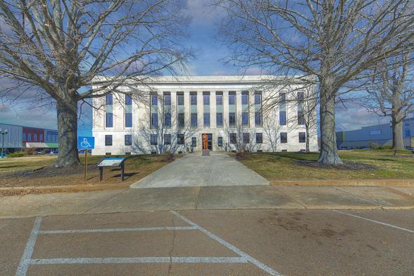 A grand courthouse with tall columns stands in the middle of the town square, framed by bare trees, evoking a sense of historical importance.