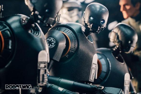 K2SO sits in the middle of two other droids of the same model. He looks directly at you. Grand Moff Tarkin and a Stormtrooper stand by in the background