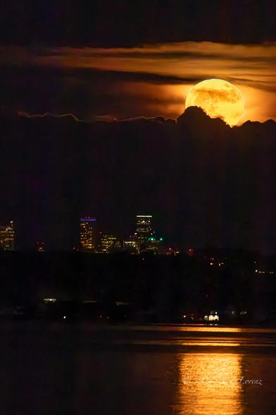 A nighttime shot of the full moon rising over Seattle and some clouds reflecting in the water.