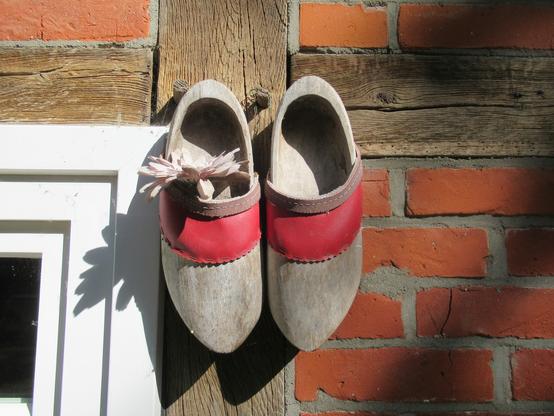 Ein Paar alter Holzschuhe an der Fassade eines Fachwerkhauses mit naturvergrauten Balken und roten Gefachen.