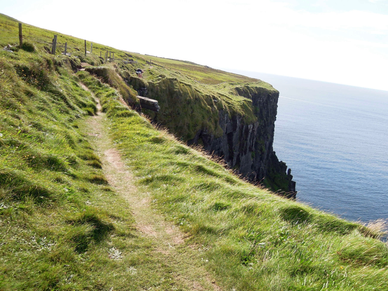 die klippen von moher … grüner bewuchs … davor blaues meer vor hellgrauem himmel