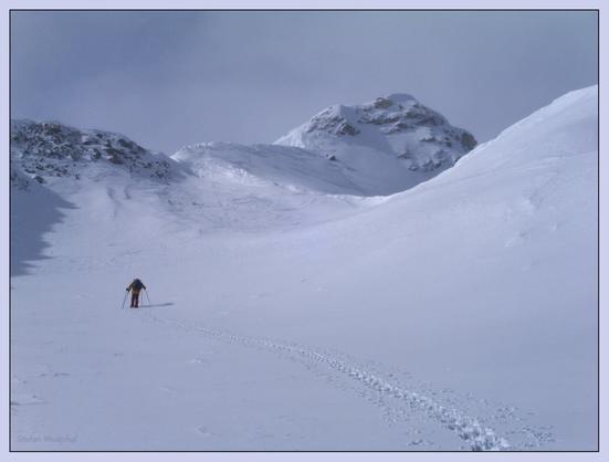 Ein einsamer Bergsteiger steigt durch eine verschneite Landschaft und hinterlässt Fußspuren. Im Hintergrund sind hohe, schroffe Berge unter einem bewölkten Himmel zu sehen. Die Szene vermittelt ein Gefühl von Einsamkeit und Abenteuer in einer winterlichen Umgebung.

A lone mountaineer ascends a snowy landscape, leaving footprints behind. Tall, rugged mountains are visible in the background under a cloudy sky. The scene conveys a sense of solitude and adventure in a winter environment.