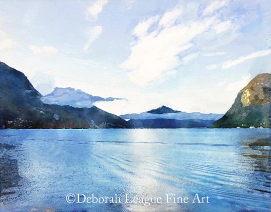 Early morning on lake Lugano, Switzerland is the view I enjoyed from my hotel room while visiting the area.

Low clouds hang over the mountains that surround lake Lugano in Switzerland. The sky, a brilliant blue, is filled with white windswept clouds. The water ripples in the light breeze, reflecting the surrounding scene.