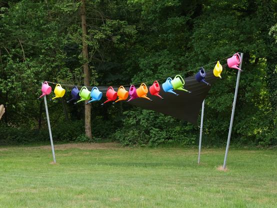 Bunte Gießkannen hängen sortiert und geordnet an einem Sonnensegel