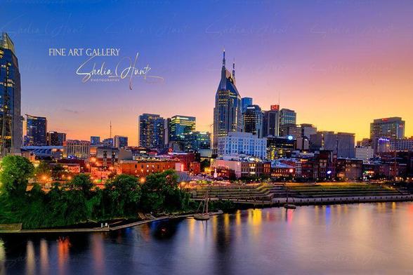 Nashville skyline at twilight with city lights reflecting on the Cumberland River, featuring iconic skyscrapers and urban charm. From the Fine Art Gallery of Shelia Hunt.