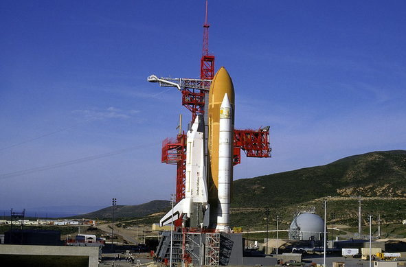 image of Space Shuttle Enterprise in vertical stacked position at Space Launch Complex 6 at Vandenberg Air Force Base in 1985. Enterprise had been the aerodynamic flight test prototype for the space shuttles. So while the spaceworthy orbiters were launched from Florida, Enterprise was used for fit checks of the launch pad at Vandenberg, even though it wasn't able to fly in space.

In archive photos of space shuttles on launch pads, any time you see terrain which is not completely flat like Florida, then you know the picture is one of the rare ones at Vandenberg in California.

US Air Force photo via Wikimedia Commons https://commons.wikimedia.org/wiki/File:Space_Shuttle_Enterprise_stacked_at_Vandenberg_SLC-6_(1).jpg

Wikimedia image caption:

Description 	
English: The space shuttle Enterprise stands fully assembled with its external fuel tank and solid rocket boosters atop America's West Coast launch facility at Vandenberg Air Force Base. The prototype orbiter was stacked at Space Launch Complex 6 in 1985 to practice procedures and check out the newly constructed pad for the Air Force's planned military space shuttle missions to polar orbit.
Date 	6 February 1985
Source 	http://www.defenseimagery.mil/imagery.html#guid=e452b1782c6486c5a36febe88191c005d4e2b66d
Author 	U.S. Air Force/TSGT Doug Gruben
Permission (Reusing this file) 	Public domain