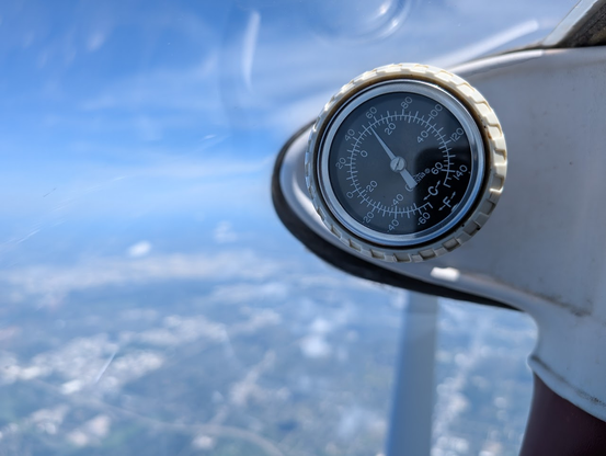 Photo of thermometer in aircraft showing outside air temperature at about 54F (12C). This was taken at 10,500 feet with a blurry Chicago behind it.