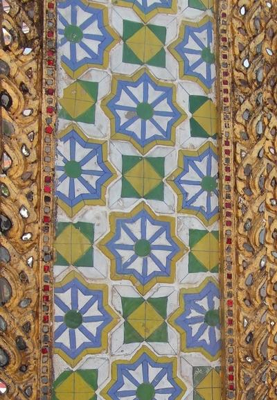 A vertical run of tiles between two ornate golden borders. The tiles are white, blue, yellow and green. The motifs are staggered eight-pointed stars and squares with green corners and a yellow centre.