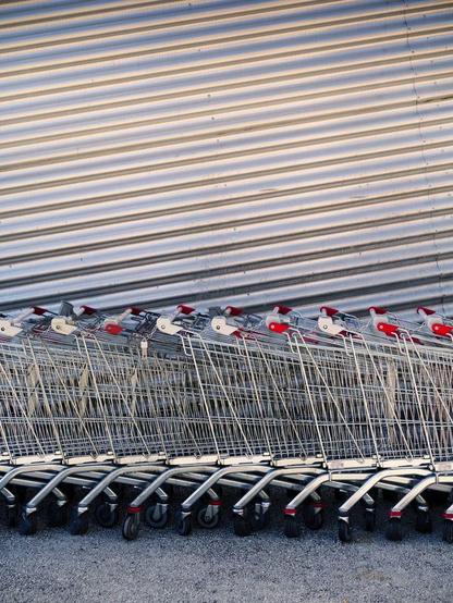 An abstract image of a line of shopping carts in front of a corrugate steel wall.
