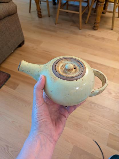A small handmade teapot with butter yellow glaze with brown spots. The lid and the curved horizontal handle on the back have more of the brown color.