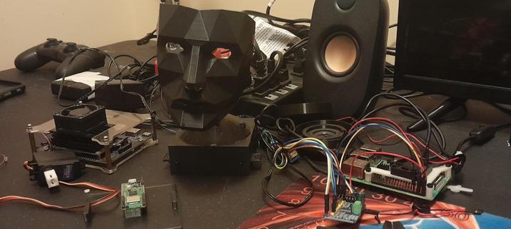 Workbench strewn with wires and smallboard computers with a 3d printed  face on a base in the center
