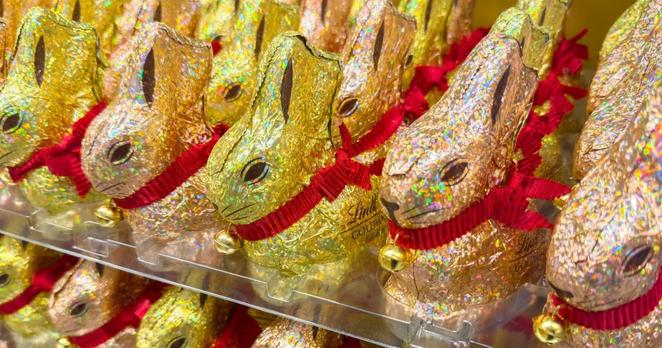 Unzählige goldgelbe und goldrötliche Osterhasen mit Glöckchen, die gut sortiert in einem Regal stehen.