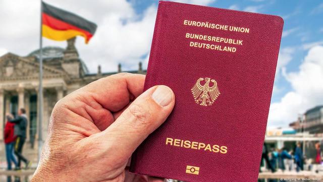 Eine Hand hält einen deutschen Pass, dahinter der Bundestag und eine deutsche Flagge