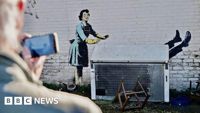 Artwork by Banksy showing a a 1950s housewife with a swollen eye, missing a tooth, and apparently shutting a man in a freezer, on the side of a house in Margate on14 February 2023