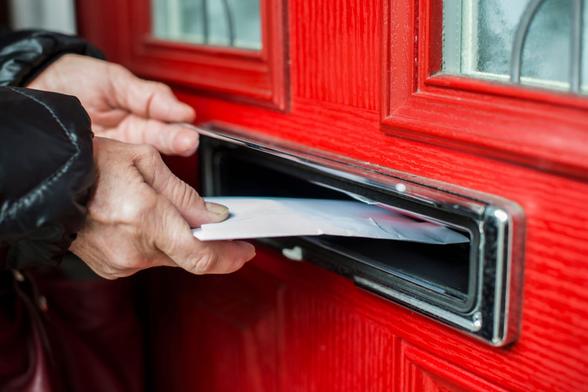 Hand steckt einen Brief in den Postschlitz einer Haustür