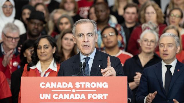 Le chef libéral Mark Carney parle au podium lors d'une conférence de presse, avec des candidats libéraux derrière lui.