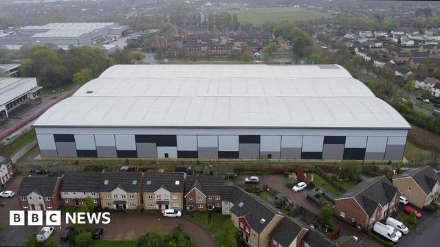 Aerial image of a massive white and blue warehouse looming over a row of houses 