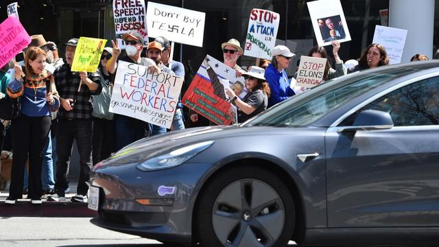 A Tesla driver stops at a stoplight as protesters hold signs in Walnut Creek, California, on Saturday, 29 March 2025, during a demonstration against Elon Musk. | Copyright AP Photo
