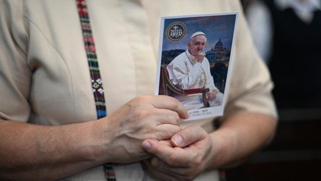 Nahaufnahme einer Frau, die ein Foto von Papst Franziskus in den Händen hält und an sich drückt.