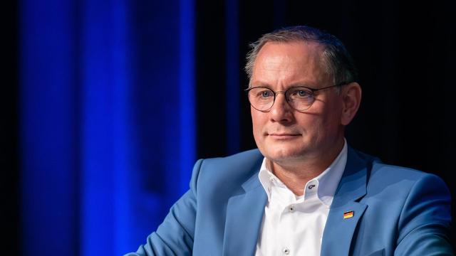 AfD-Bundesvorsitzender Tino Chrupalla in hellblauen Anzug mit weißem Hemd vor blauem Hintergrund.