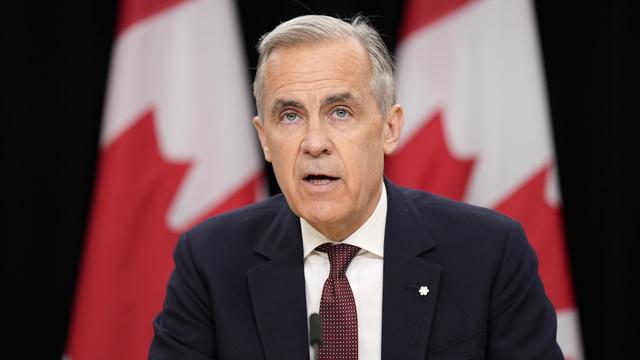 Le premier ministre Mark Carney lors d'une conférence de presse devant des drapeaux canadiens.