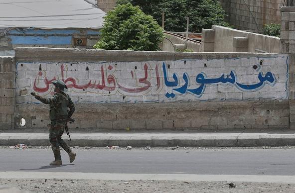 A Syrian government security forces gunman passes in front of an Arabic graffiti that reads "From Syria to Palestine", Jaramana, Damascus, Syria, Wednesday, April 30, 2025 (AP)