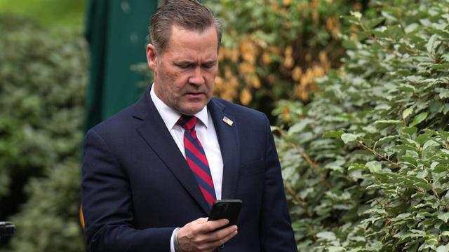 National Security Advisor Michael Waltz stands outside next to some trees or bushes while looking down at his phone. National Security Advisor Michael Waltz stands outside next to some trees or bushes while looking down at his phone.