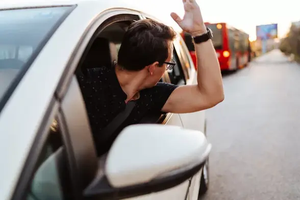 Ein Mann schaut aus einem Autofenster und hebt die linke Hand.
