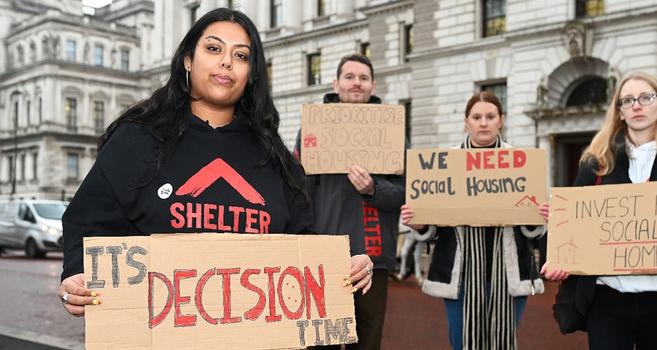 Four Shelter campaigners are outside holding various messages: ' It's decision time', 'Prioritise social housing', 'We need social housing', and' Invest in social housing'. Four Shelter campaigners are outside holding various messages: ' It's decision time', 'Prioritise social housing', 'We need social housing', and' Invest in social housing'.