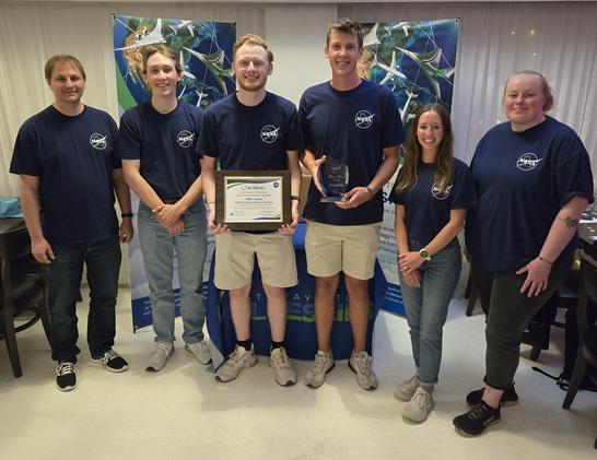 Group photo of the South Dakota State University team wearing blue NASA t-shirts standing in front of two Bannerstands after winning 2025 Gateways to Blue Skies.