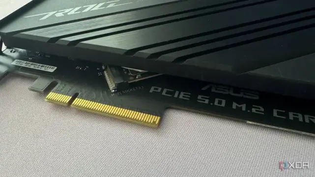 Close-up of an ASUS PCIe 5.0 M.2 expansion card with a sleek black heatsink and gold connectors, showcased on a light background.