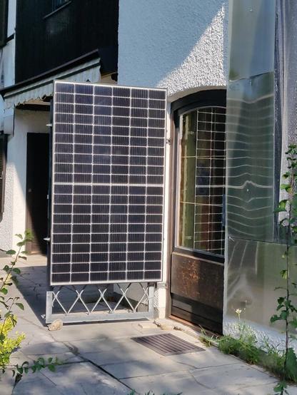 Das Foto zeigt eine Hausfassade mit Terrassentür. An einem schmiedeeisernen Ziergitter für die Terrassentür wurde ein PV-Modul befestigt. Das Gitter ist etwa halb aufgeschwenkt, so dass das Modul genau der Sonne entgegen schaut. Am Boden ist das Gitter fixiert, indem es zwischen auf dem Boden liegende Steine eingeklemmt ist.
Das Bild soll mein Verständnis von "Gamification" ausdrücken: durch manuelles Nachfahren an den Sonnenstand wird der Bruchteil einer Kilowattstunde dazugewonnen, wirtschaftlich ist der Aufwand also durch nichts zu rechtfertigen, der Stundenlohn für die Tätigkeit bewegt sich wohl im zehntel-Cent-Bereich.
