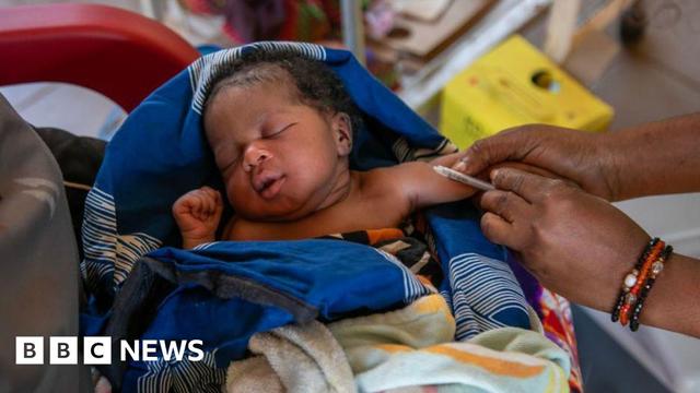 A young baby wrapped in a blue blanket receives a vaccination in Senegal in 2024