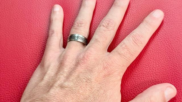 A caucasion hand wearing a silver band on their ring finger.