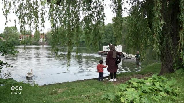 A woman and a child hold hands as they look over a lake