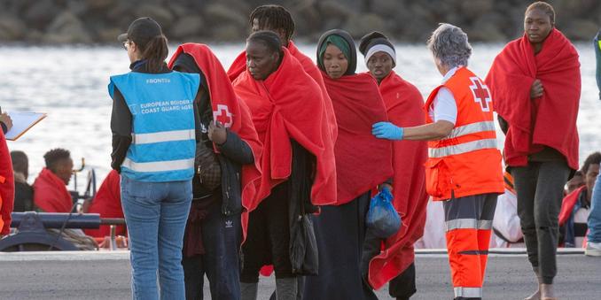 A Frontex agent, wearing a blue vest, stands at the arrival of migrants rescued from drowning by a Spanish sea rescue unit, at the Port of Arrecife, Spain, on 3 January 2025. | ADRIEL PERDOMO/EPA