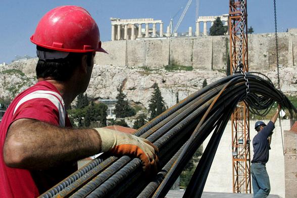 Ein Bauarbeiter trägt Stahlstangen, im Hintergrund die Athener Akropolis