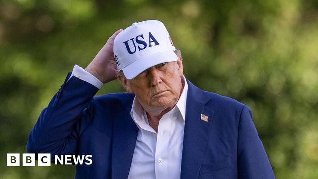 US President Donald Trump wearing a blue suit and a white cap with USA on it