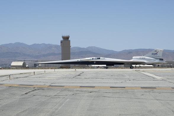 NASA’s X-59 aircraft taxis on the runway at U.S. Air Force Plant 42 in Palmdale, California. The aircraft is shown in profile moving from right to left, with the control tower and desert mountains in the background. In the foreground, the gray concrete runway features a solid yellow line with evenly spaced parallel black stripes inside it, all under a clear blue sky. NASA’s X-59 aircraft taxis on the runway at U.S. Air Force Plant 42 in Palmdale, California. The aircraft is shown in profile moving from right to left, with the control tower and desert mountains in the background. In the foreground, the gray concrete runway features a solid yellow line with evenly spaced parallel black stripes inside it, all under a clear blue sky.
