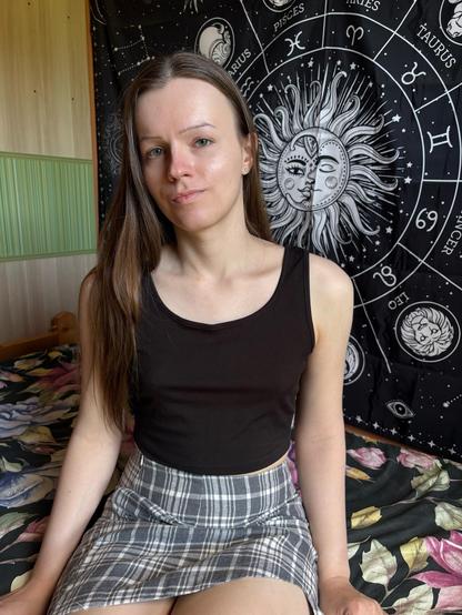 Photo of me sitting on bed. I’m wearing a black tank top and plaid miniskirt.