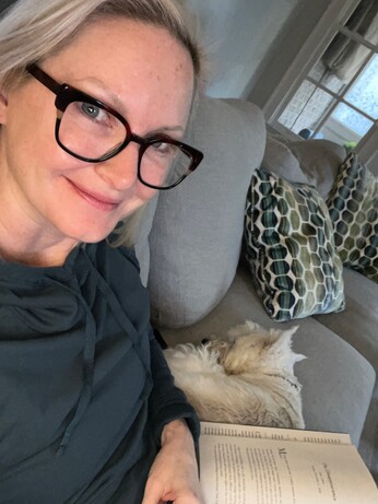 Woman on couch w dog and book in her lap