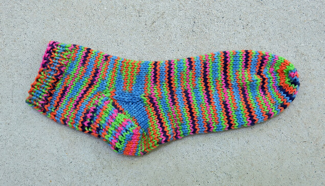 Short colorful sock, made with DK yarn. Electric pink, blue and green with black interspersed. Unfortunately, I cannot remember which yarn and which pattern I used. 
