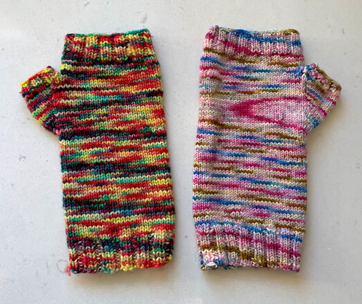 Fingerless gloves made with Malabrigo yarns. On the left, a sport yarn (Arroyo) in yellow, red, navy and green yarn and on the right, a sock yarn in pink, blue, brown and white.