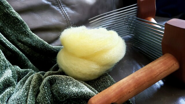 A birds nest of finished roving next to a set of wool combs.