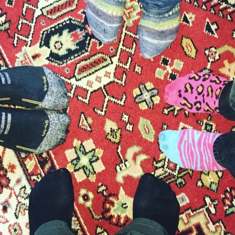 4 Paar Füsse in bunten Socken im Kreis stehend auf bunten Teppich